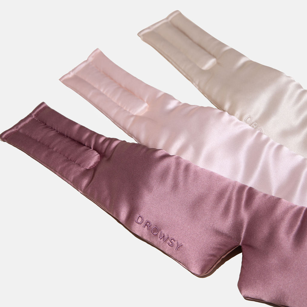 Three luxury silk masks from Drowsy’s Besties Pack in cream, light pink, and mauve are laid out overlapping. Made from mulberry silk for ultimate beauty sleep, the mauve mask in front features ‘DROWSY’ embroidery.