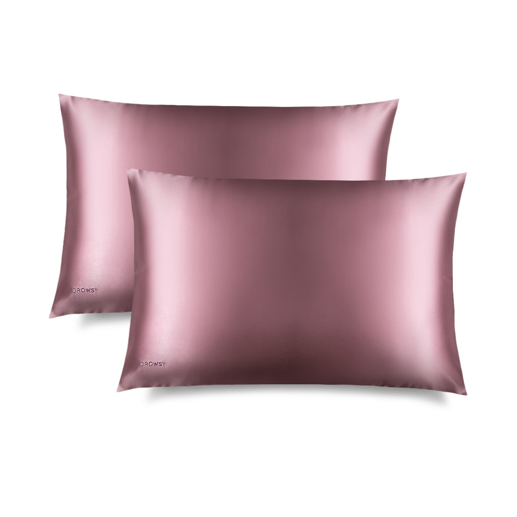 Two smooth, shiny Damask Rose Silk Pillowcases by us.drowsysleepco are stacked with one slightly overlapping the other. Each features a subtle logo in the bottom left corner, perfect for hair protection and skincare. The background is plain white.