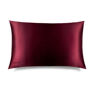 The La Vie En Rouge Silk Pillowcase by us.drowsysleepco is a rectangular burgundy silk case with a smooth, shiny finish and a subtle embroidered logo in the bottom left corner, displayed against a white background. Perfect for protecting hair.