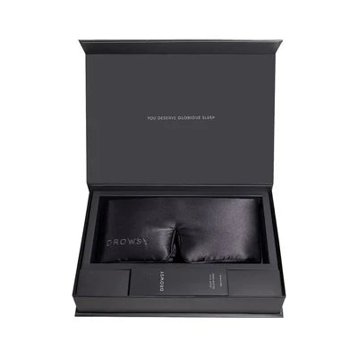 A black gift box with a satin sleep mask and a rectangular accessory inside, both labeled Drowsy, and the lid reads You deserve glorious sleep in white text.
