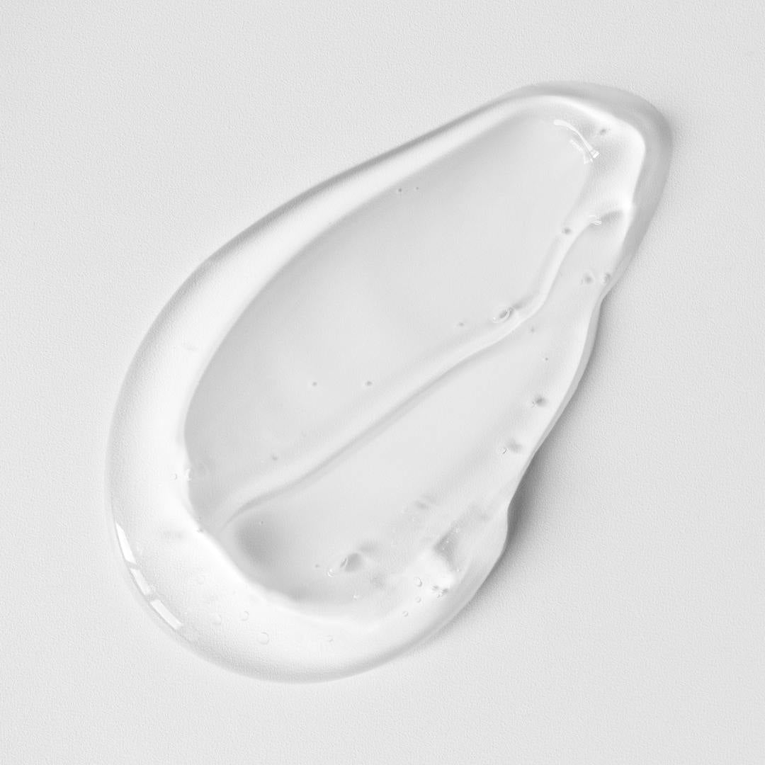 A clear, glossy gel with tiny bubbles—us.drowsysleepcos Beauty Sleep Body Cleanser with calming magnesium—is spread in an uneven teardrop shape on a smooth white surface.