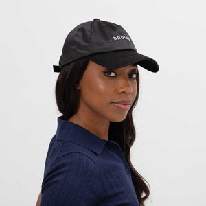 A woman wearing the Drowsy Silk Cap - Black Jade by Drowsy and a navy blue collared shirt faces sideways, looking at the camera against a plain white background—ideal for outdoor workouts.