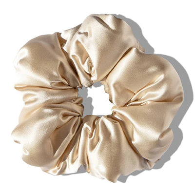 A large, shiny beige silk scrunchie with gathered fabric, forming a circular shape, photographed on a white background with a soft shadow.