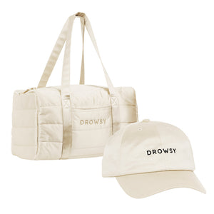 The Drowsy Roadtrip bundle – Dusty Gold features a beige duffel bag and matching cap with 'DROWSY' in black on the front, displayed against a white backdrop—ideal for travel, style, and hair care.
