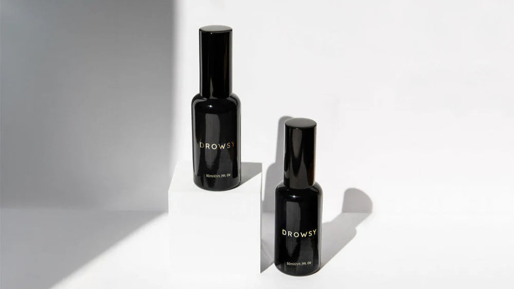 Two black bottles labeled DROWSY are displayed on a white surface, with one bottle elevated on a small white block. The background is white with subtle shadows.