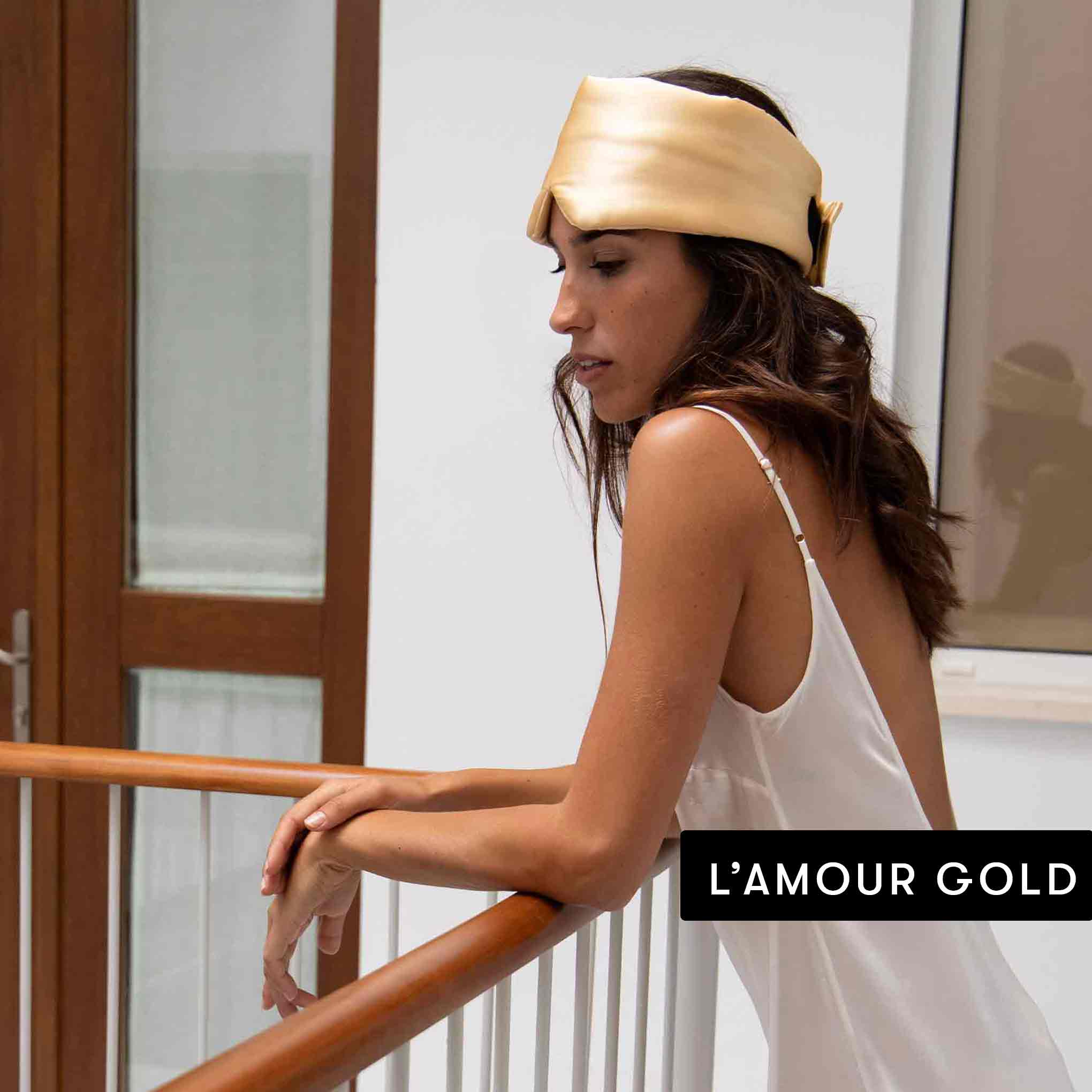 A woman in a white satin slip dress leans on a wooden railing, wearing a shiny mulberry silk headband from the Lovers Pack by Drowsy. The text LAMOUR GOLD appears in the lower right corner.