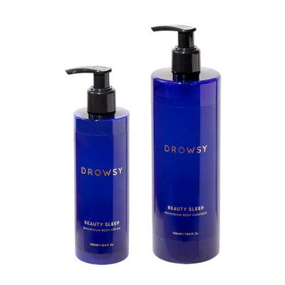 Two blue pump bottles labeled “Drowsy Beauty Sleep.” The smaller bottle is body cream and the larger is body cleanser. Both have black pumps and gold text on the labels.
