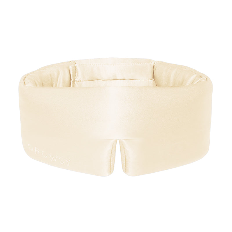 The us.drowsysleepco Champagne Gold silk eye mask features a cream hue, plush padding, a wide band, and a contoured bottom to block light and promote deep beauty sleep.