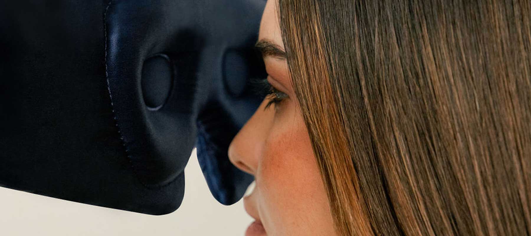 A woman with straight brown hair rests her face against the padded surface of a dark blue pillow or relaxation device, covering her eyes and nose.