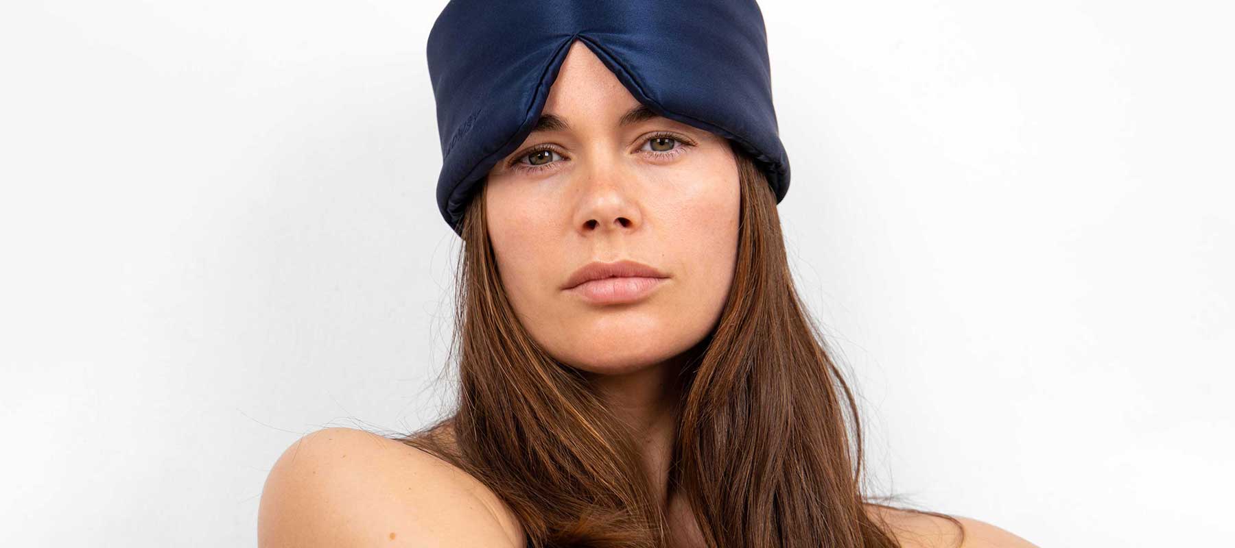 A woman with long brown hair wears a navy blue satin headwrap and looks directly at the camera against a plain white background.