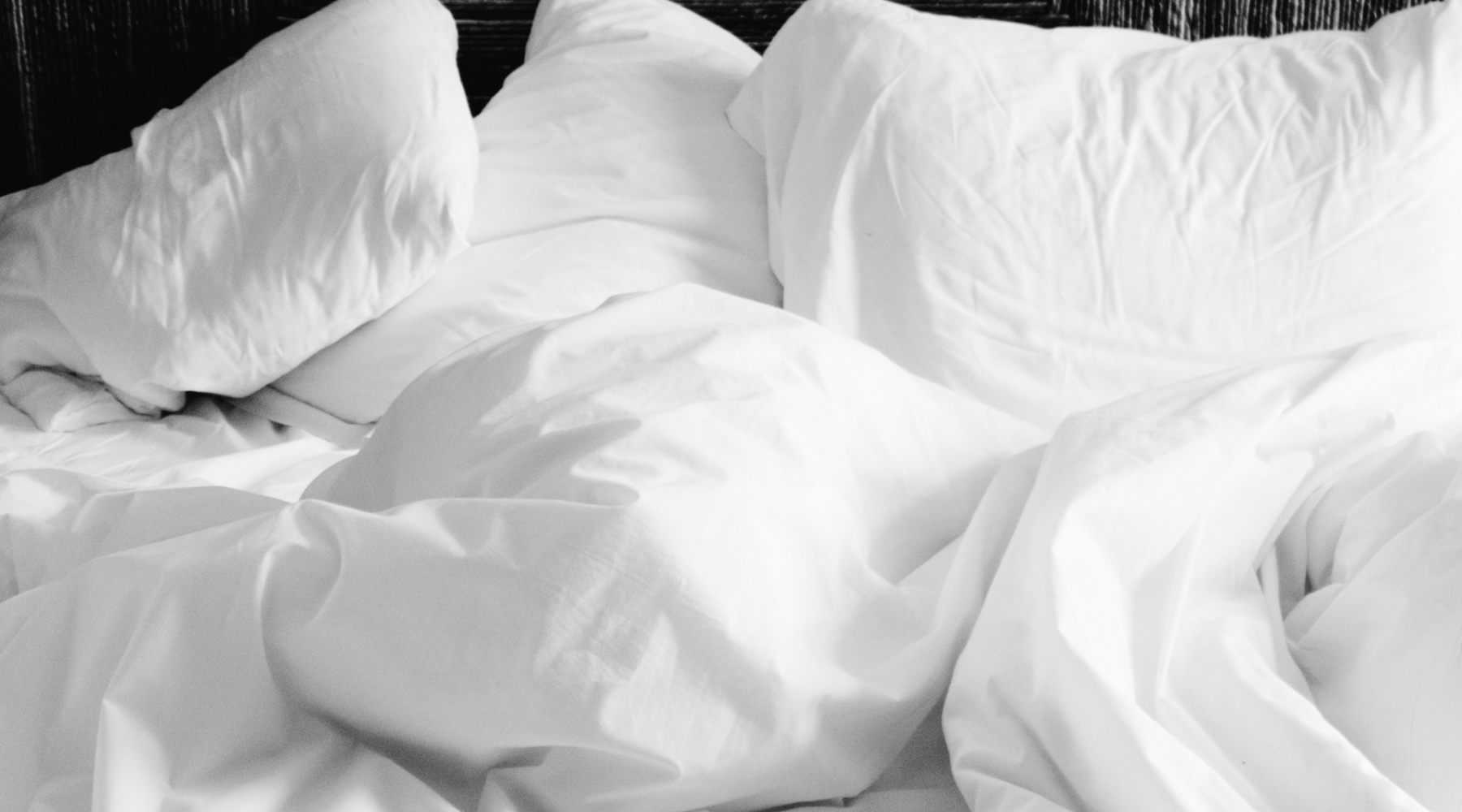 Messy bed with white pillows and white bedsheets.