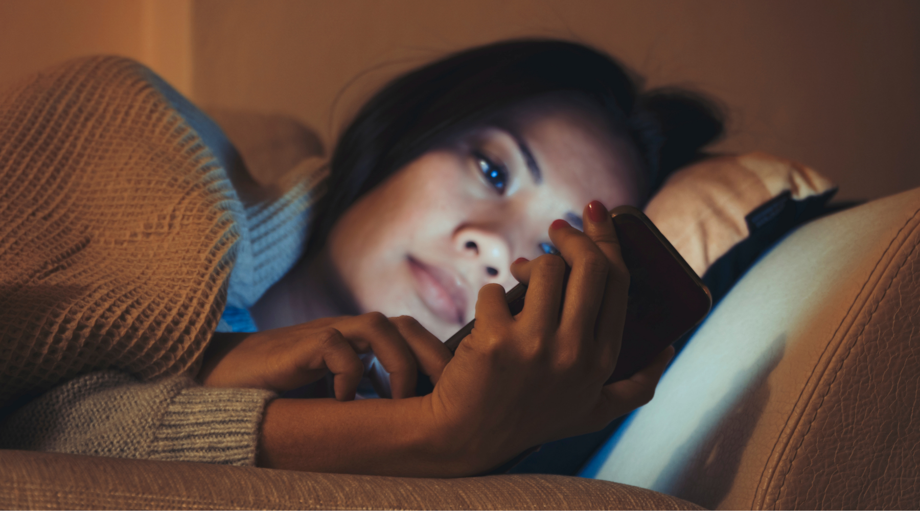 Girl lying in bed scrolling on mobile phone.