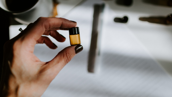 Hand holding small brown bottle with a desk in the background.