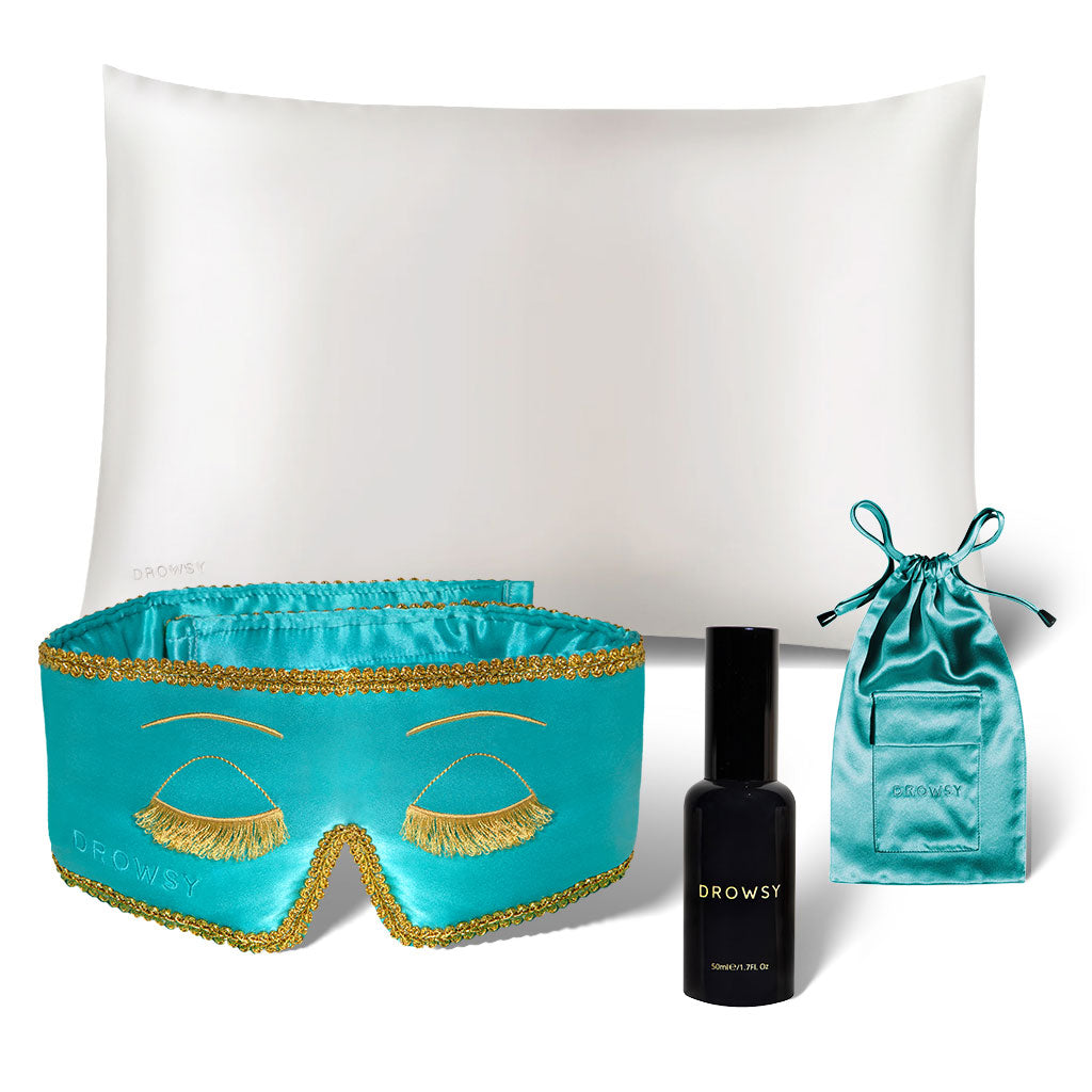 The Breakfast at Drowsy Beauty Bundle by drowsysleepco features a white pillow, silk sleep mask with gold trim, black Drowsy spray bottle, and turquoise pouch—all displayed against a white background.