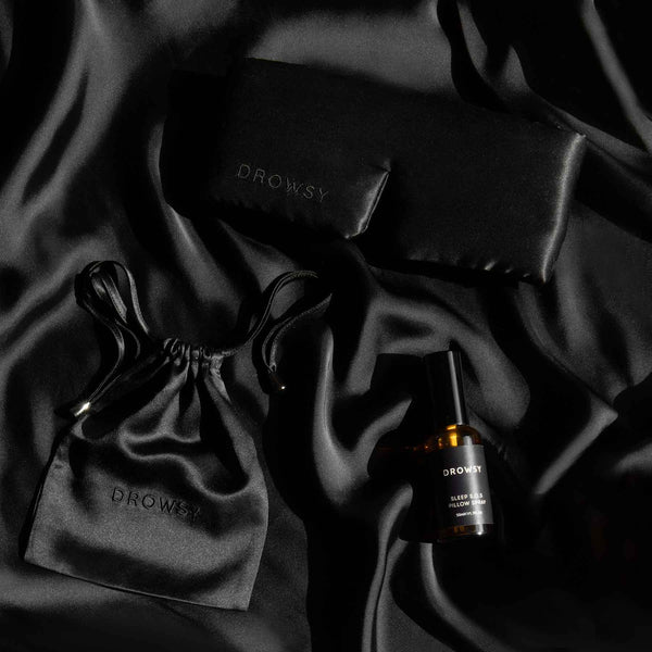 Black sleep mask, black silk pouch and pillow spray on black silk background