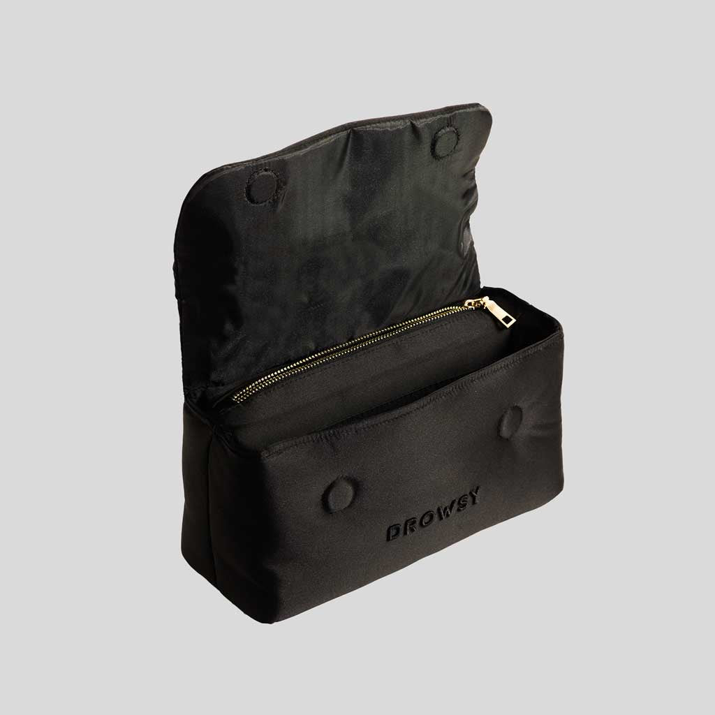 The Drowsy Silk Necessaire - Black Jade by Drowsy is a black fabric pouch with an open top flap, zippered compartment, snap button closure, and embroidered logo—ideal for elevating your beauty routine. Light gray background.