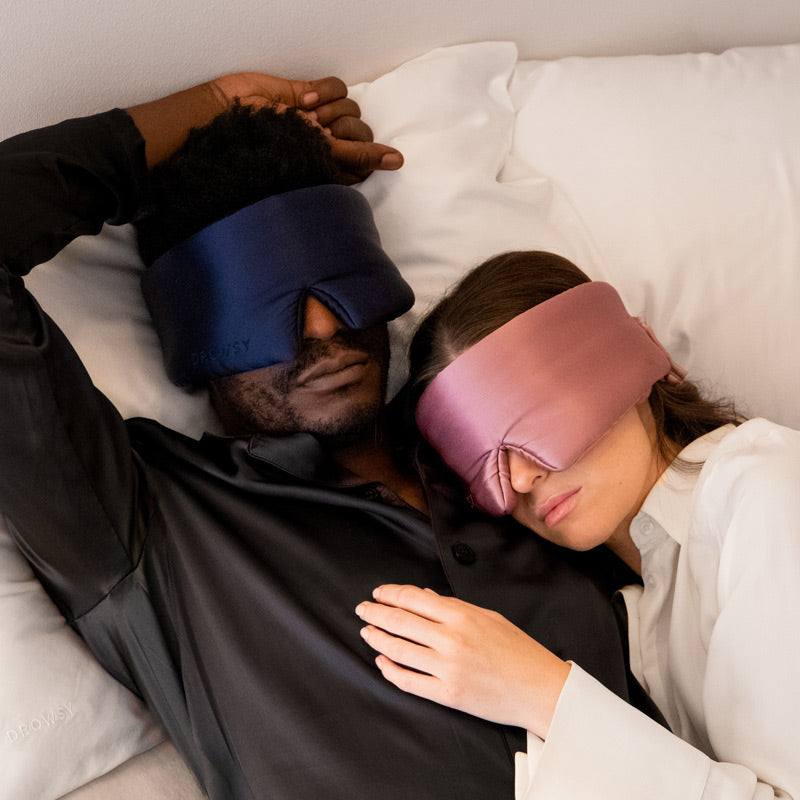 A man and woman lie in bed wearing drowsysleepco 2-Pack Sleep Masks in Midnight Blue and Damask Rose, enjoying restful nights together.