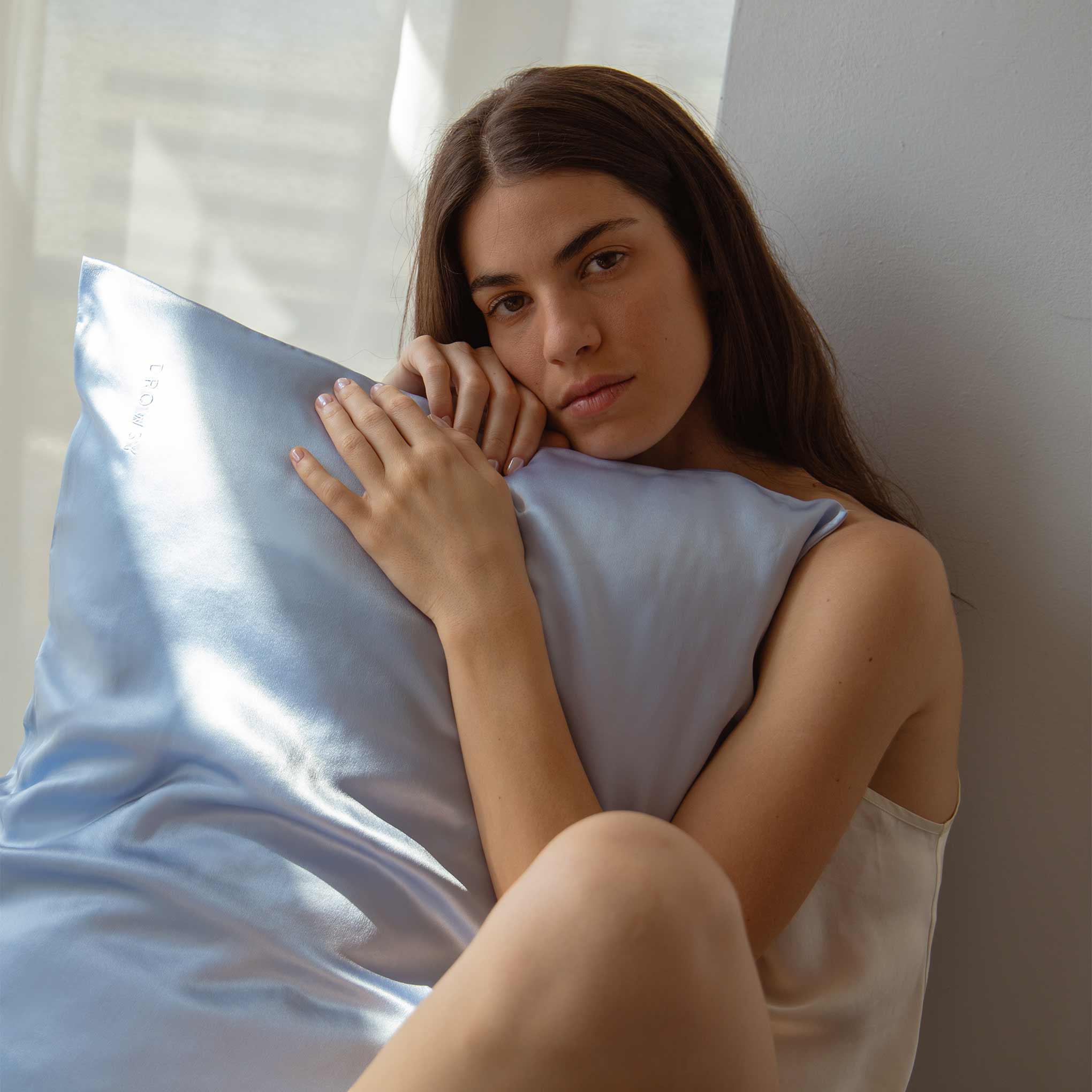 Model hugging a baby blue Drowsy silk pillowcase