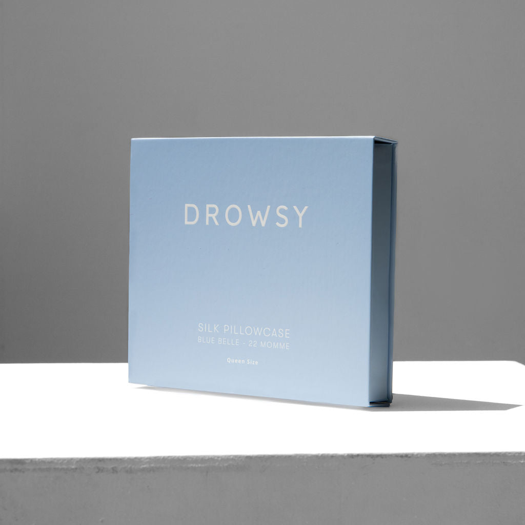 Baby blue coloured Drowsy silk pillowcase box on a white stand with a grey background