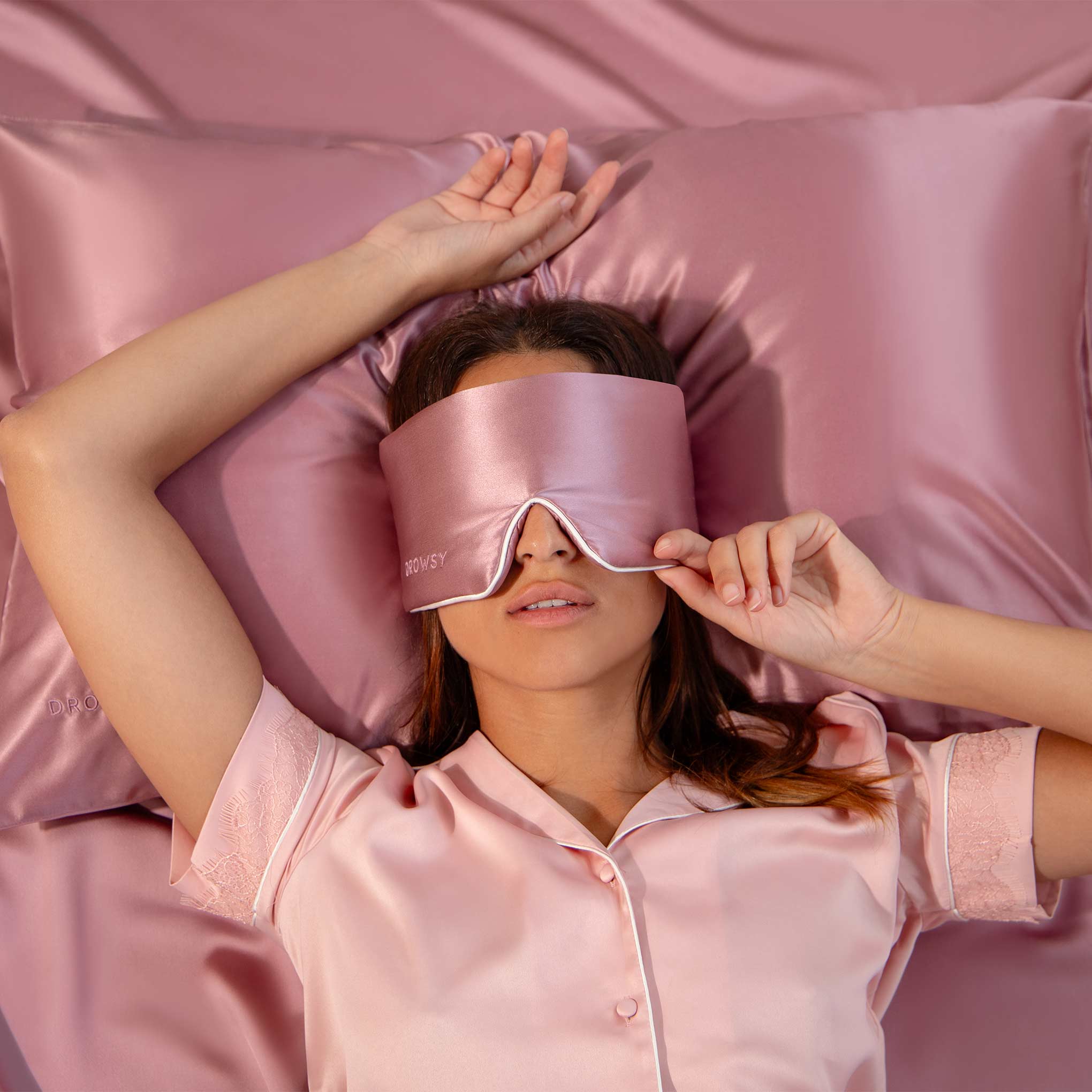 Model sleeping on pink Drowsy silk pillowcase with pink Drowsy silk sleep mask covering her eyes