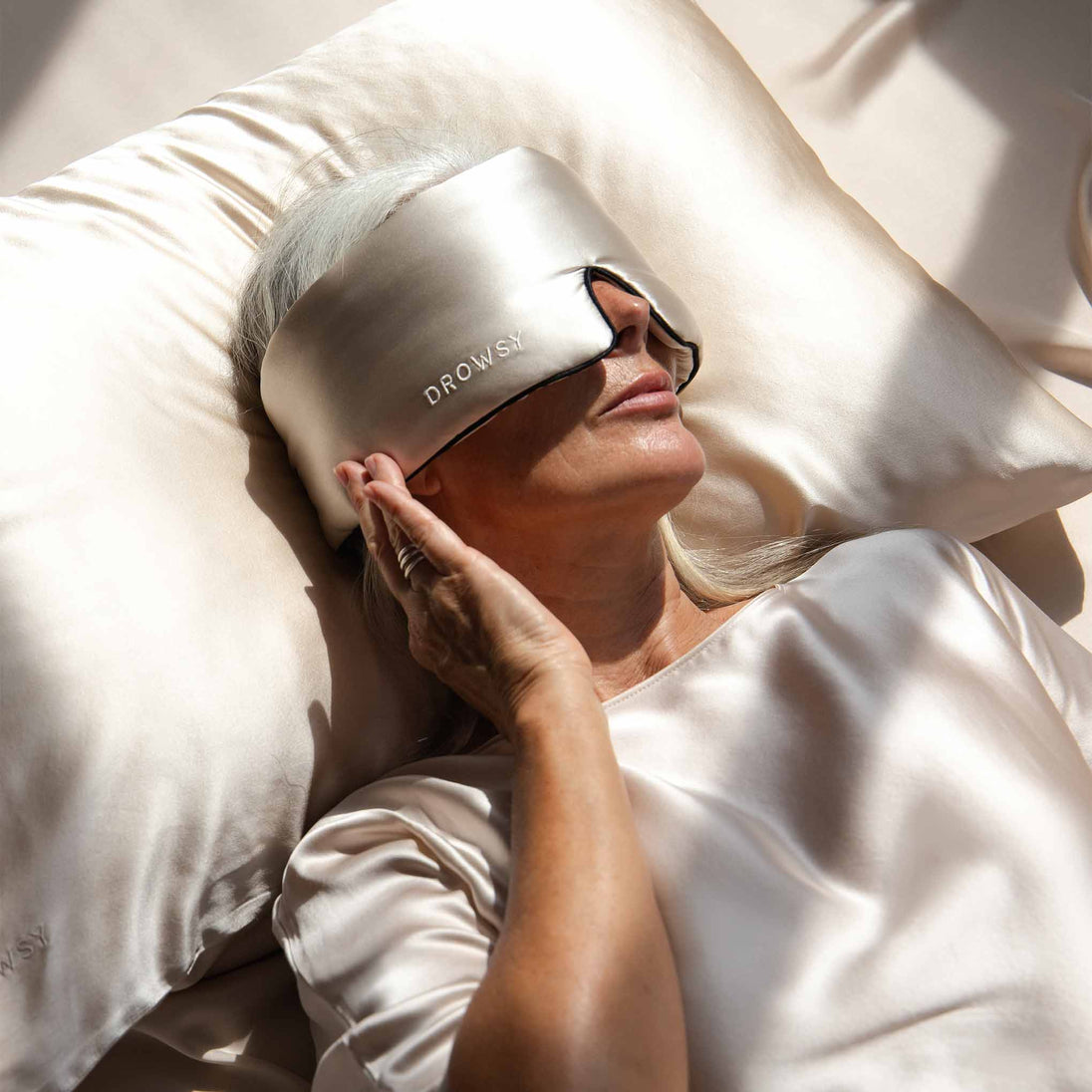 Woman sleeping on a dusty gold coloured Drowsy silk pillowcase with a Drowsy silk sleep mask covering her eyes