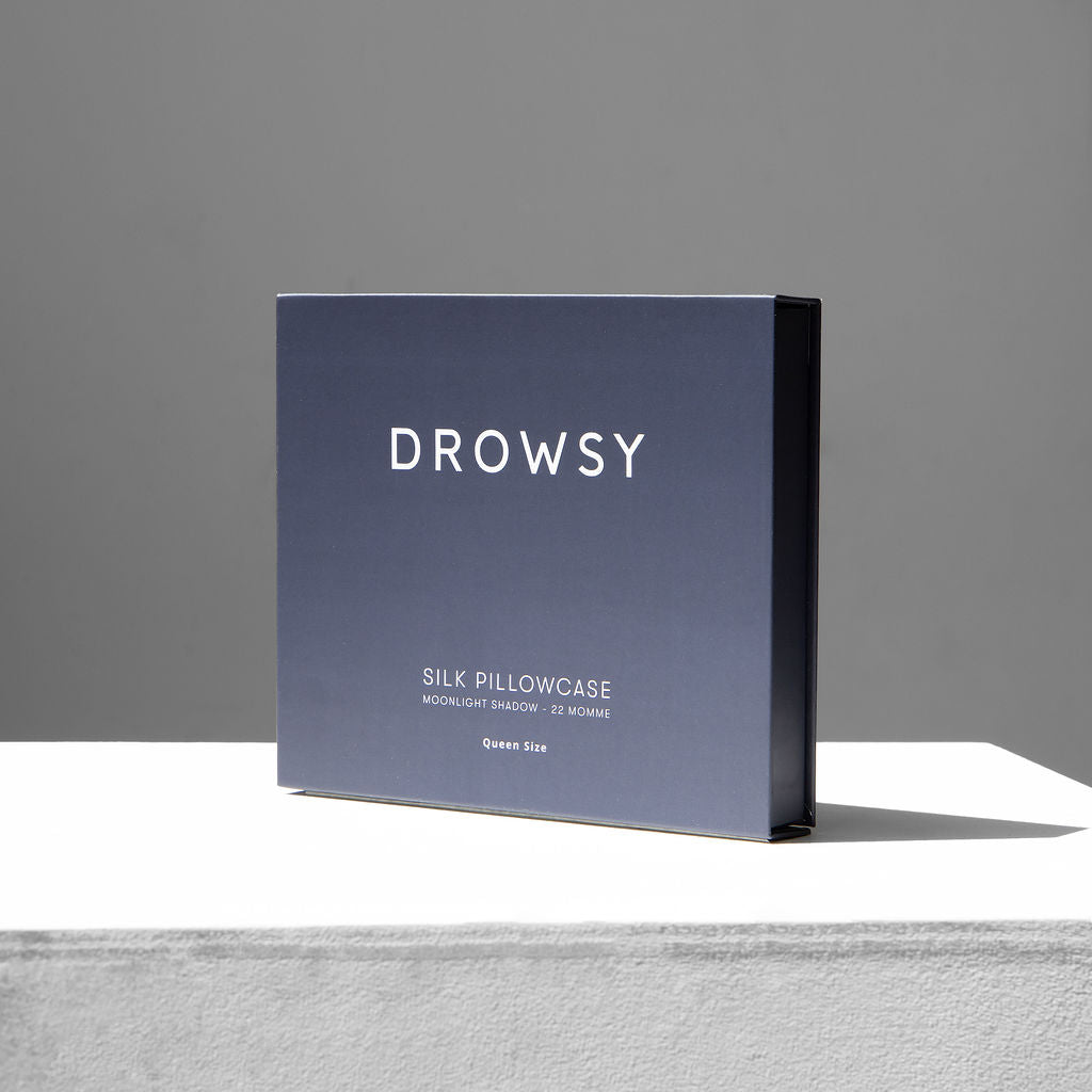 Charcoal coloured Drowsy silk pillowcase box on a white stand with a grey background