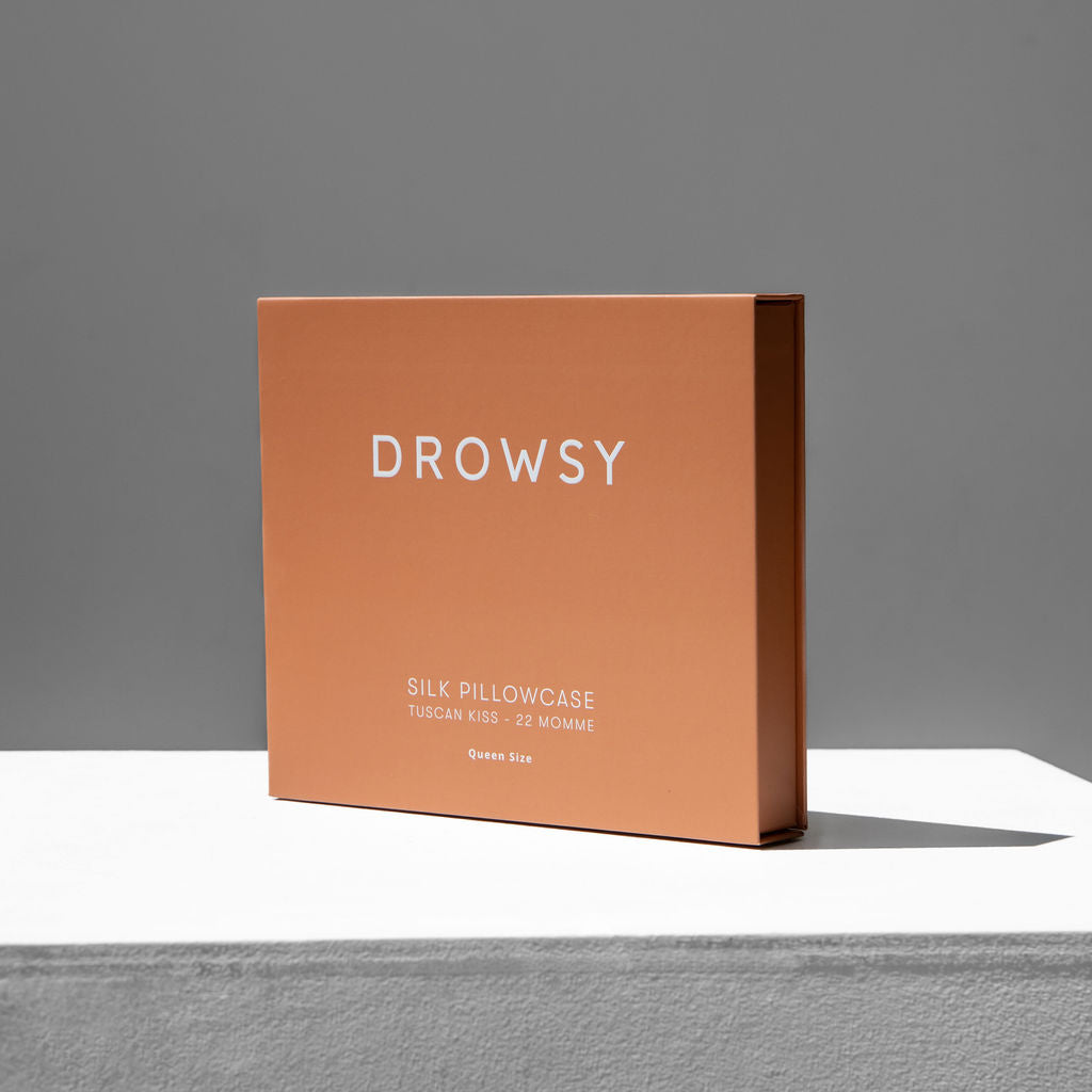 Terracotta coloured Drowsy silk pillowcase box on a white stand with a grey background