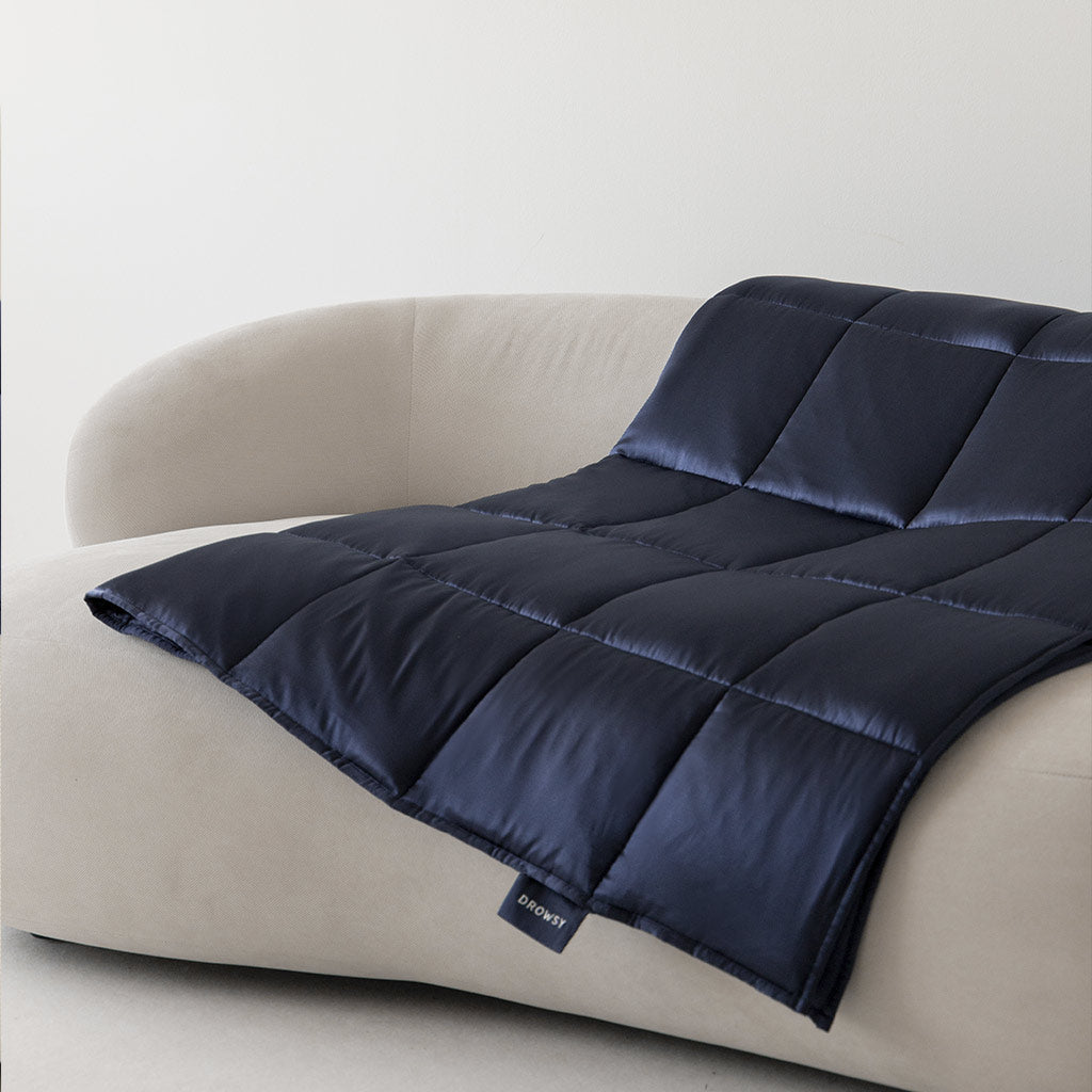 A navy blue quilted blanket is draped over a curved, light beige sofa against a plain white wall.