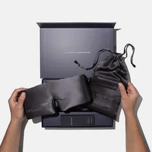 Two hands hold the Moonlight Shadow - Deep Sleep Collection by us.drowsysleepco: a luxury silk sleep mask and pouch above a gift box with deep sleep pillow spray. Inside the lid reads "YOU DESERVE GLORIOUS SLEEP.