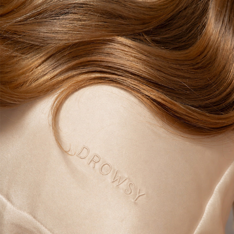 Close-up of silky brown hair resting on a Hyalo Pillowcase in Champagne Gold by us.drowsysleepco, with “DROWSY” subtly embroidered into the luxurious beige fabric.