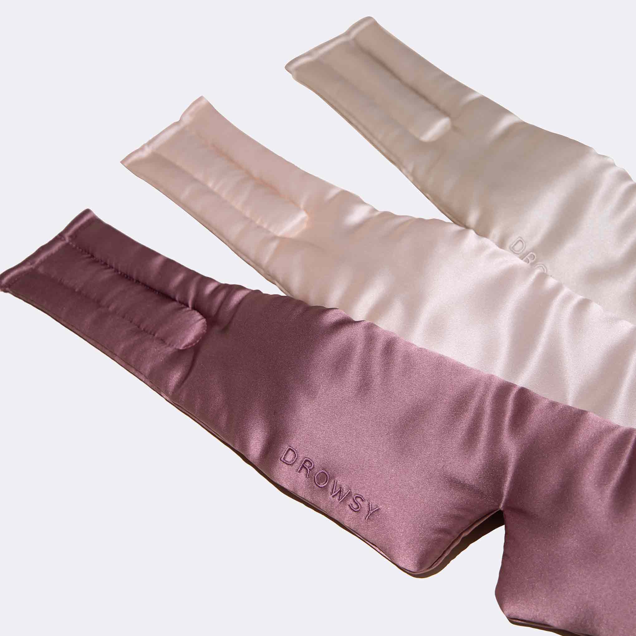 The Besties Pack by us.drowsysleepco features three silky luxury masks in mauve, light pink, and cream—each embroidered with DROWSY—arranged on a plain background to elevate your beauty sleep.