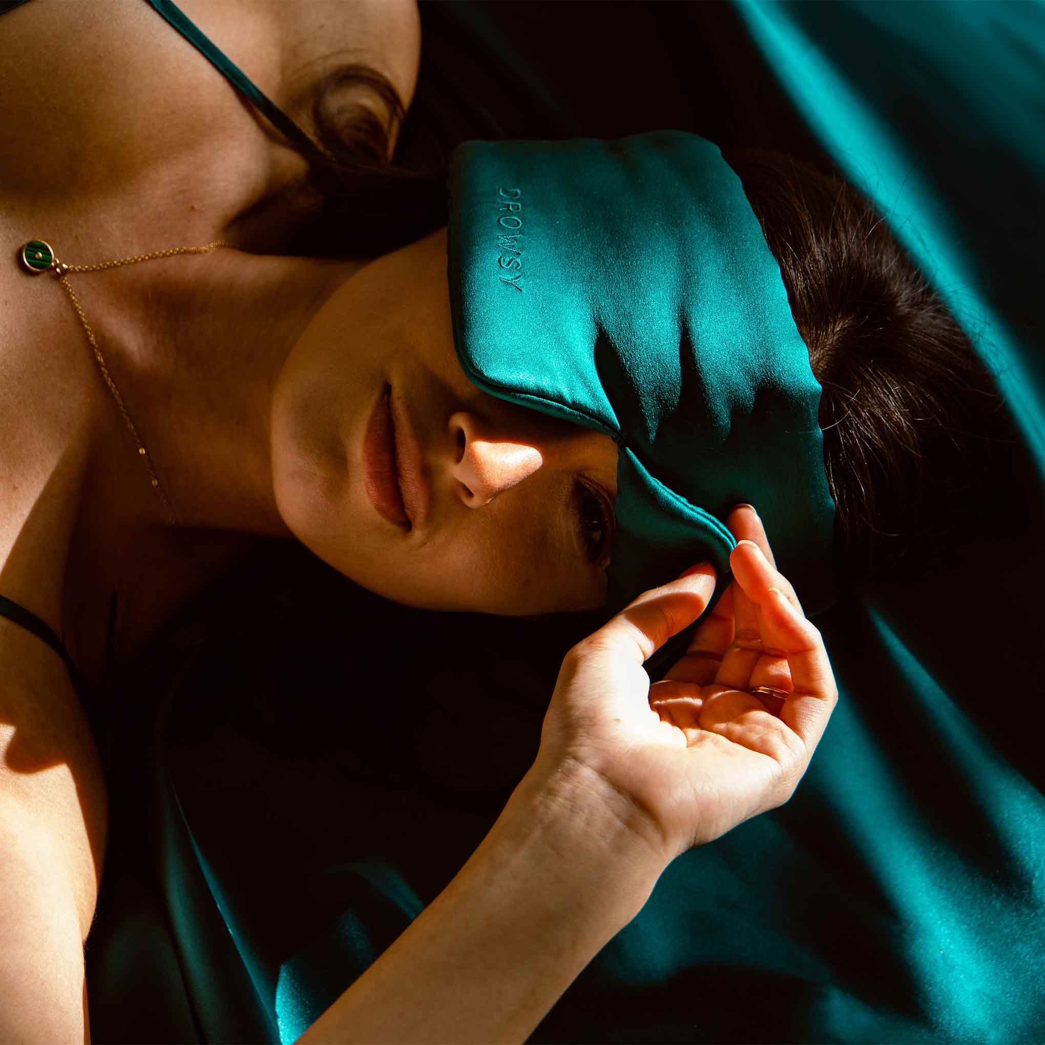 Girl sleeping on green silk with Drowsy Silk Sleep Mask covering eyes